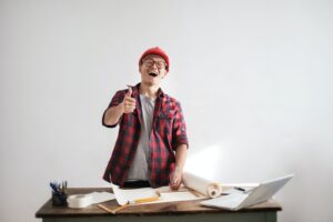 Laughing male constructor showing thumb up at working desk